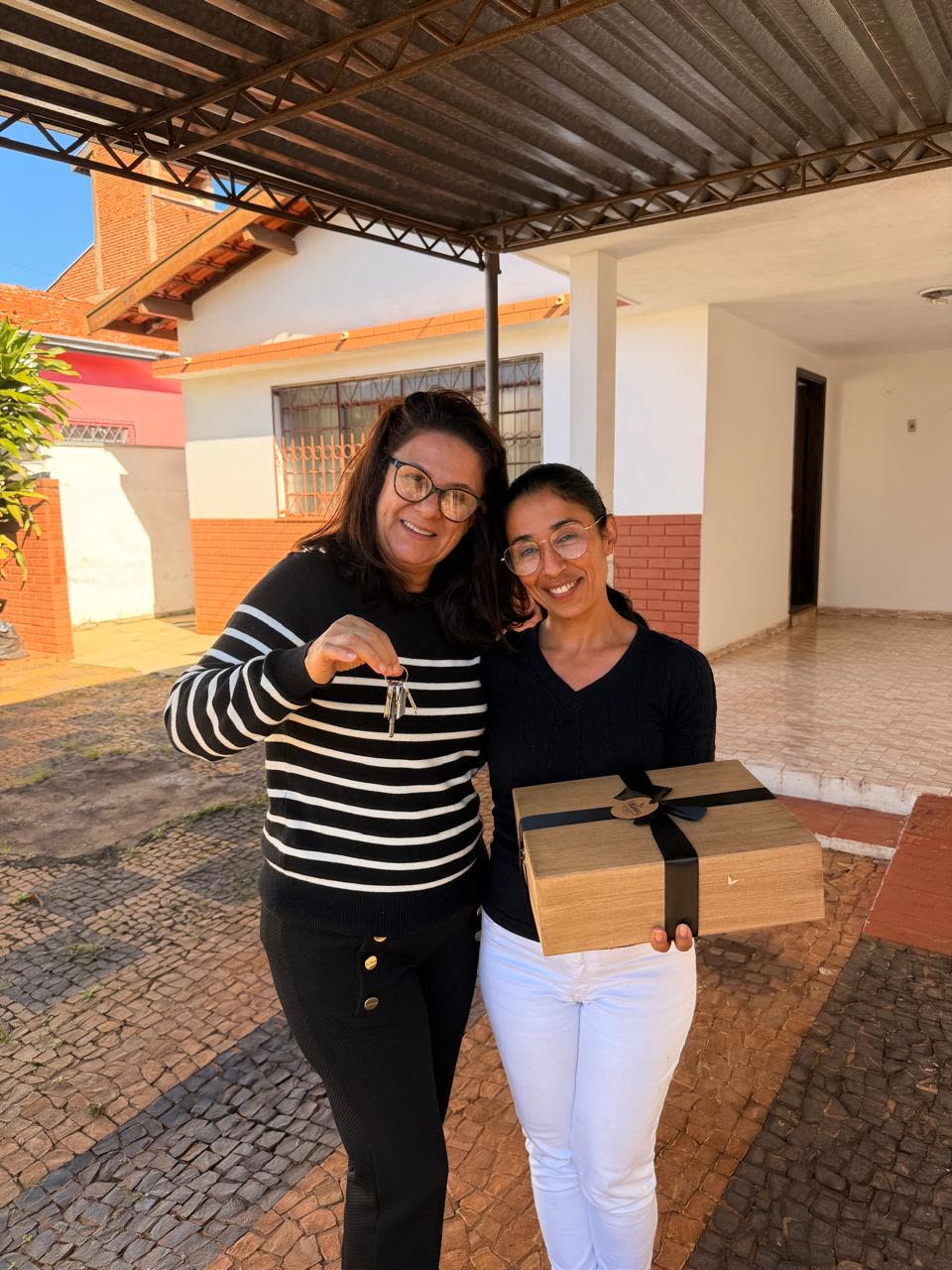 Corretora entregando a chave e um presente de boas-vindas na porta do novo imóvel